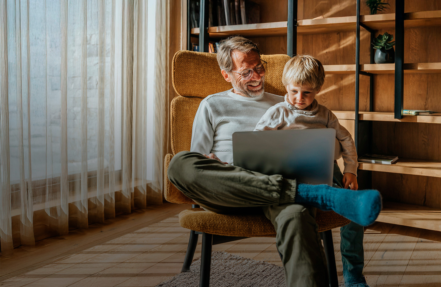 Ein Mann sitzt mit einem Kind auf einem Sessel und die beiden Schauen in einen Laptop